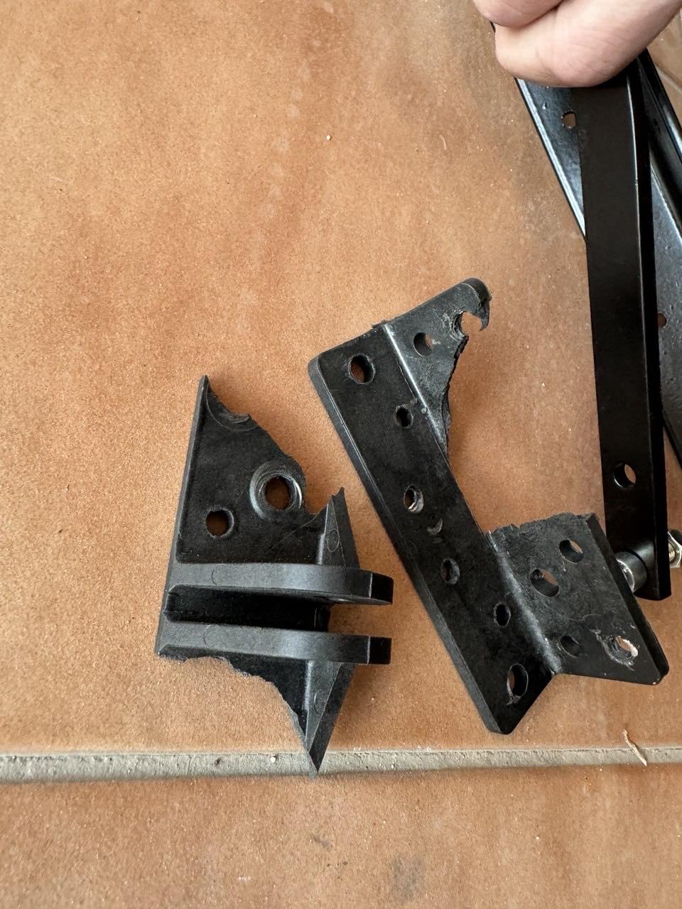 Two broken factory brackets next to the new one