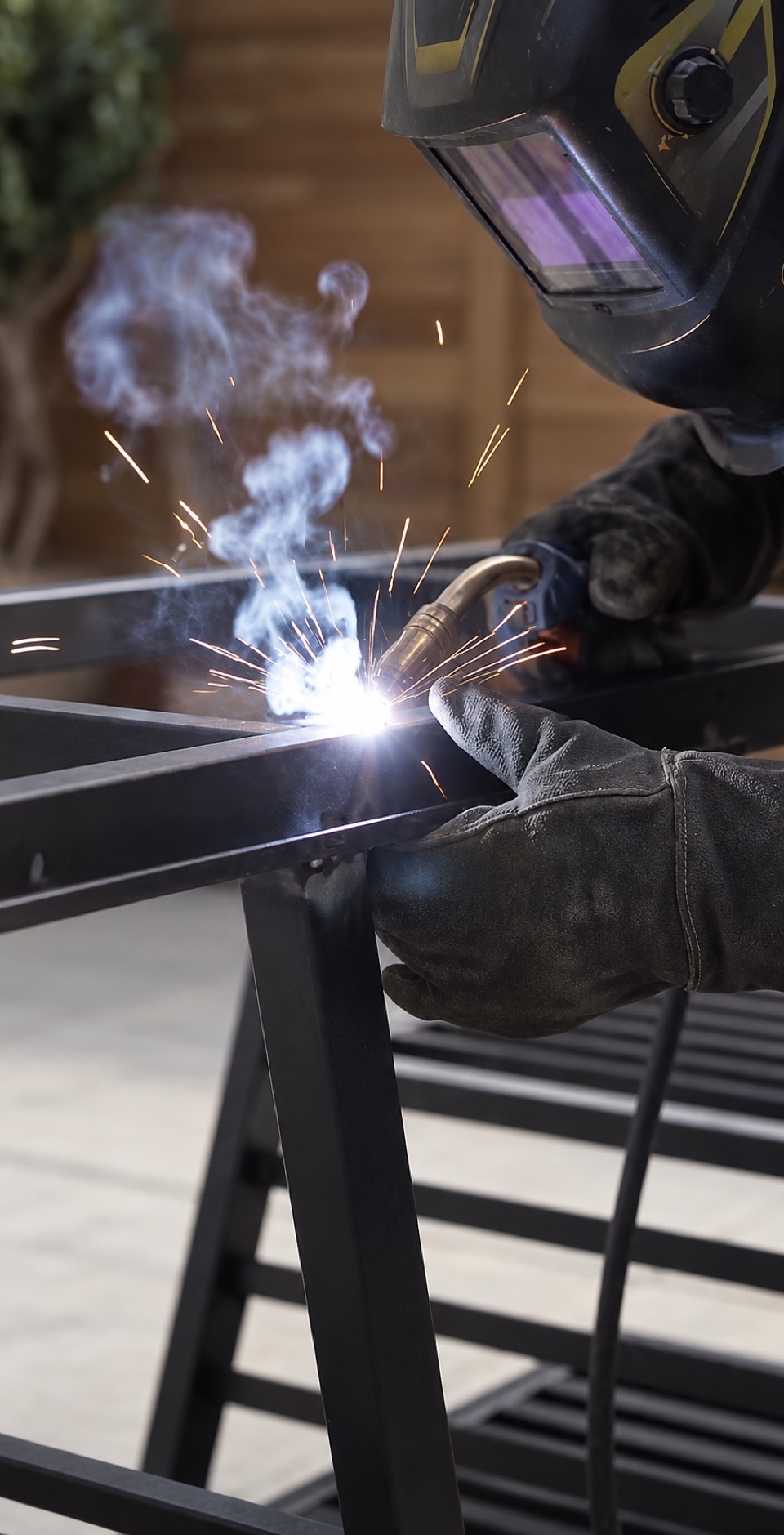 Welder in a protective mask welding a steel frame in the workshop